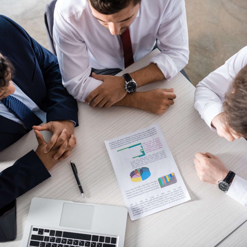 Overhead view of professional businessmen discussing charts at workplace, business concept